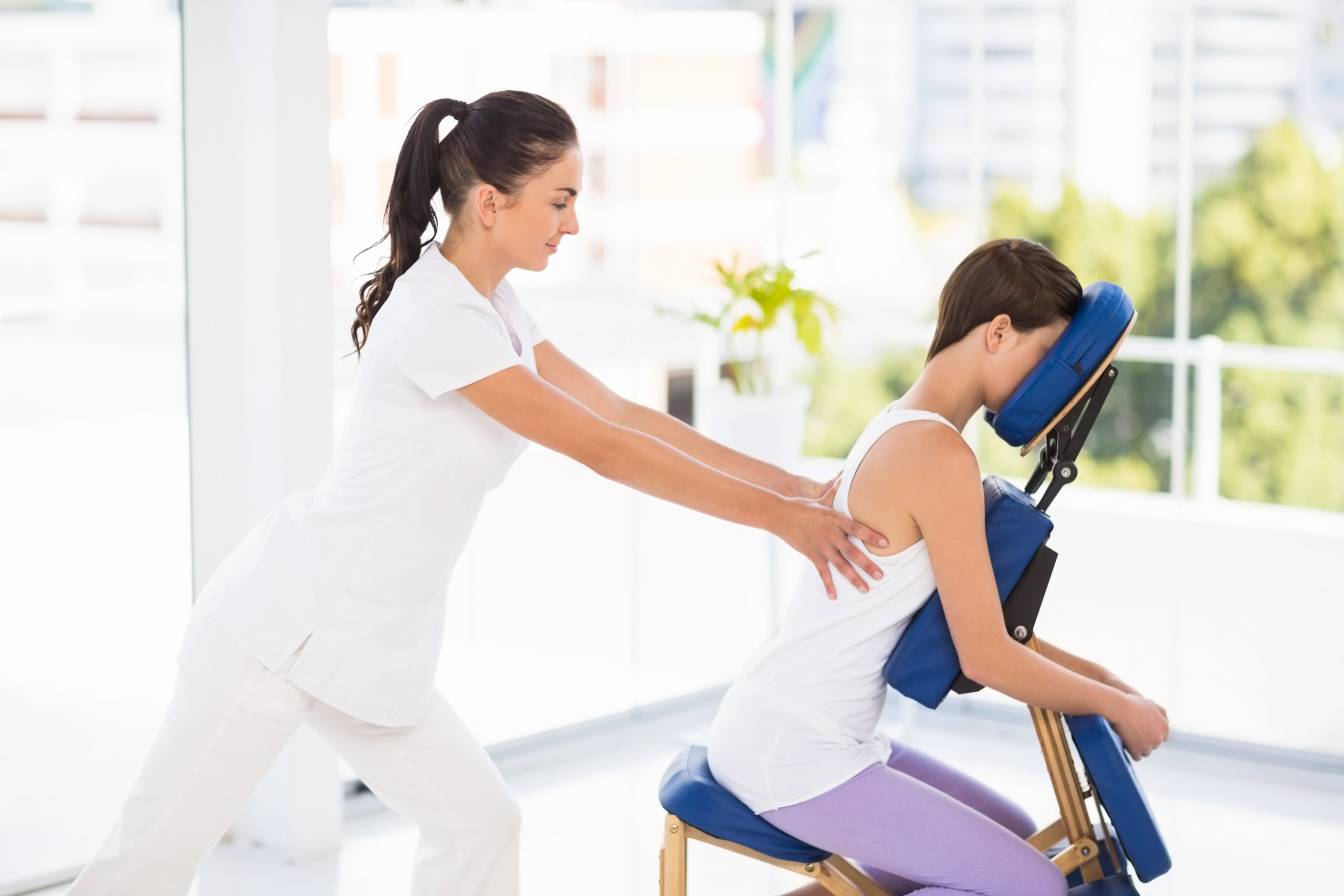 Woman being massaged on chair by masseuse at spa