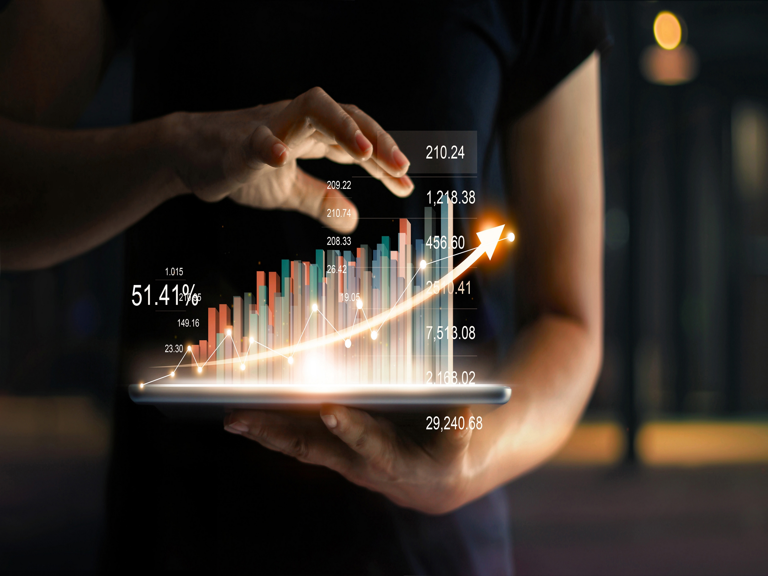 businessman holding tablet and showing a growing virtual hologram of statistics, graph and chart with arrow up on dark background. Stock market. Business growth, planing and strategy concept.