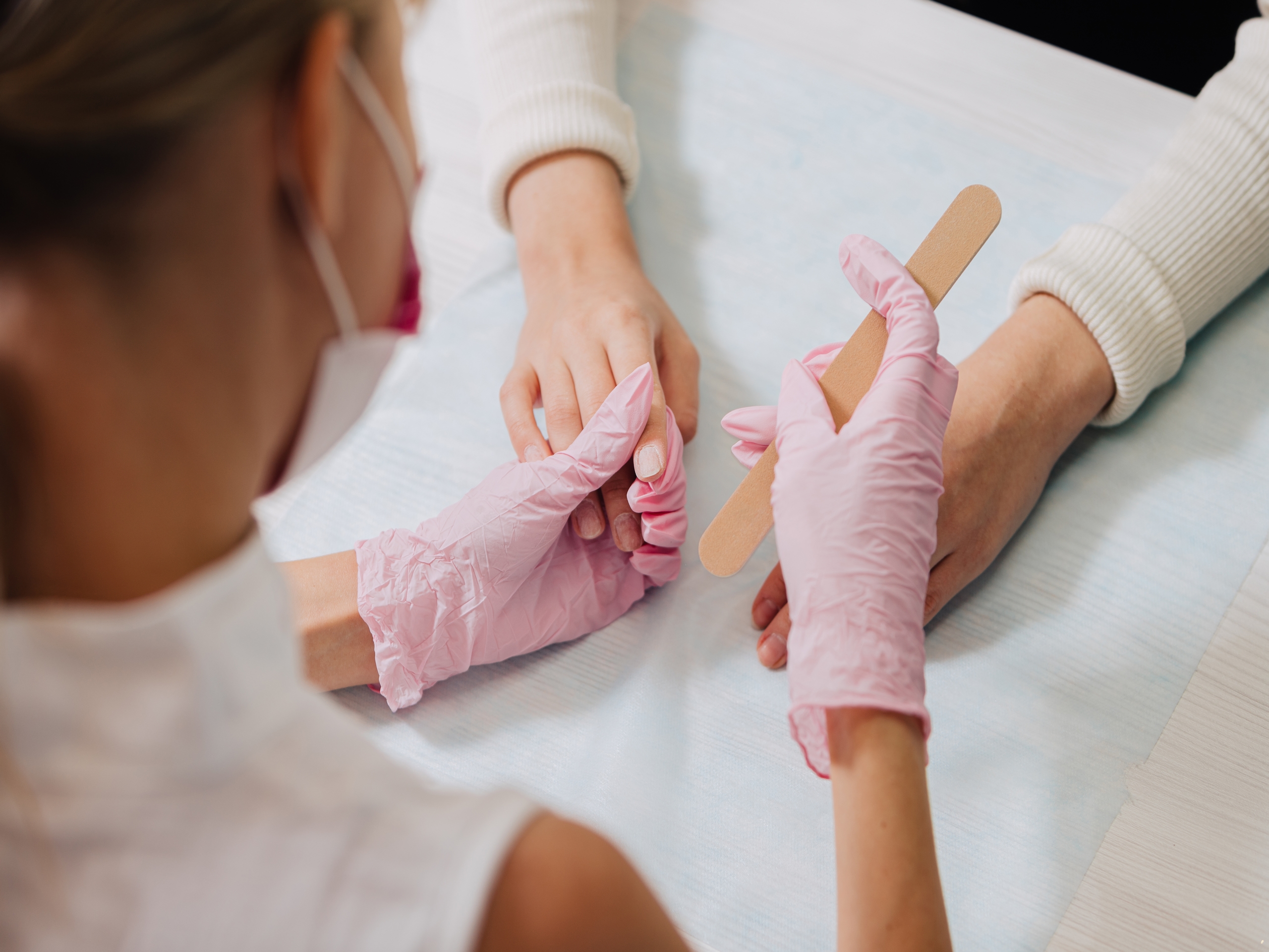 Manicure process. A master in pink rubber gloves processes the nails with a nail file. Female hands close up.